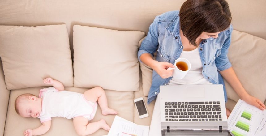 Top view of young woman is working at home and drinking tea while her little baby is sleeping.